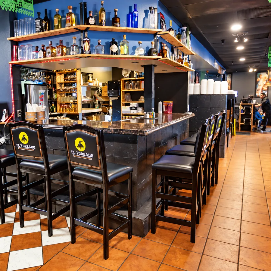 The El Toreado bar with branded high-back stools, a stocked tequila shelf and checkered tile floor