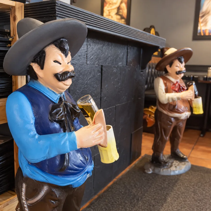 Two hand-painted charro statues holding beer mugs beside the El Toreado host stand